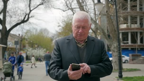 Пожилой Человек Идет Городу Прикасается Своему Мобильному Весной Замедленной Съемке — стоковое видео