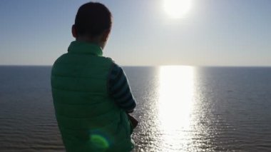 Karadeniz suları yavaş gün batımında parlayan, düşünceli çocuk görünüyor çarpıcı bir arkadan görünüm çizgili tişört Karadeniz ayakta ve yavaş hareket yaz aylarında sihirli günbatımı bakarak küçük bir çocuk