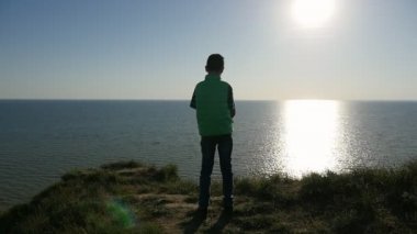 Mavi Karadeniz yavaş gün batımında çizgili tişört içinde küçük bir çocuğun bir arty arkadan görünüm Karadeniz ayakta ve yaz ağır çekimde pitoresk günbatımında bakarak dalgalar rüya gibi çocuk bakar