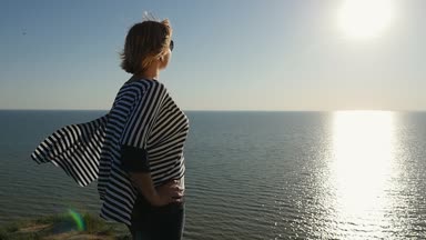 Rüya gibi sarışın kadın yavaş profil bir sallayarak büyüleyici bir kadının bluzu ve slo-mo güneş yolu ile altın bir günbatımında Karadeniz sahilde duran güneş gözlüğü çizgili gün batımında Karadeniz sahilinde durumda