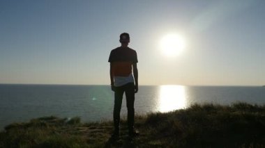 Sportif genç adam Karadeniz kıyısında Karadeniz kıyısında ayakta ve slo-mo gün batımında muhteşem güneş yol zevk pantolon slo-mo arka görünümünde çizgili tişört, iyimser bir adamın parlayan batımında standları