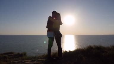 Tutkulu çift yaz aşık bir adam, Karadeniz ağır çekimde parlayan güneş yolu ile muhteşem bir günbatımı, ince sevgilisi öpüşme profil Karadeniz sahilinde muhteşem bir günbatımı öpüşme
