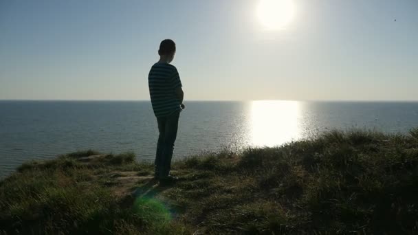 ロマンチックな少年を見てください輝く黒海でスローモーションの印象的な日没波ストライプ シャツを着た小さな男の子の背面黒海に立っているとスローモーションで夏の素晴らしい夕日を見てください — ストック動画