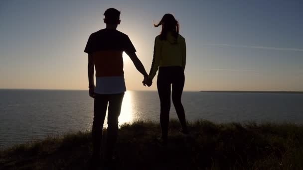 一对相爱的情侣在夏季的黑海海岸享受着一个艺术的日落 在一个浪漫的男人的放大 在一个灿烂的日落 在黑海的光辉的太阳路径保持他的女朋友的手 — 图库视频影像