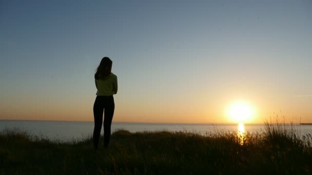 苗条的女人站在黑海海岸 看着金色的日落后 一个浪漫的女孩在牛仔裤和衬衫站在黑海海岸 并考虑到她的爱在日落与一个美丽的太阳路径夏天 — 图库视频影像