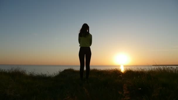 年轻女子站在黑海海岸 看着华丽的日落后看到一个梦中的女孩穿着牛仔裤和一件上衣站在黑海海岸 享受阳光灿烂的道路在夏季日落的看法 — 图库视频影像