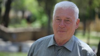 İyimser yaşlı adam standları ve yaz bir neşeli gri başlı adam ayakta, neşeyle gülümseyen ve bir yeşil sokak yaz aylarında güneşli bir hayattan zevk onun 80'li yıllarda portresi bir sokakta mutlulukla gülümser
