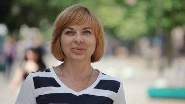 Çok güzel sarışın kadın standları ve güneşli bir günde mutlu sarışın bir kadın ayakta ve neşeyle yaz aylarında güneşli bir günde bir park sokakta gülümseyen bob saç kesimi ile çizgili bir bluz içinde Closeup park sokakta gülümsüyor