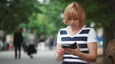 Akıllı sarışın kadın het yaz Bokeh portre güzel bir sarışın kadının park sokakta onun smartphone üzerinde yeşil bir parkta onun hareket eden bazı bilgi yaz aylarında güneşli bir günde isteyen bob saç modeli ile sörf