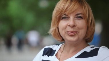 Mutlu sarışın kadın bir tezgah ve gülümsüyor yeşil bir parkta yaz neşeli ve zarif bir sarışın kadın Closeup park arka sokakta bir bankta oturmuş ve mutlu bir şekilde yaz aylarında güneşli bir gülümseyen bob saç modeli ile oturur
