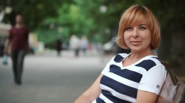 Yaz park sokakta ahşap bir bankta oturmuş ve mutlu bir şekilde yaz aylarında güneşli bir gülümseyen neşeli ve şık sarışın bir kadın portresi bir tezgah ve gülümser bir park sokakta çekici sarışın kadın oturuyor