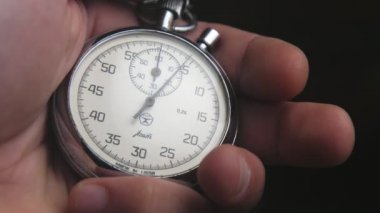 Erkek el, iki saat yüzlü retro-görünüm kronometredeki düğmeye basar. Bir erkeğin iki beyaz saat yüzü, iki daire çizen ok ve siyah sayılar içeren klasik görünümlü bir kronometrede gümüş bir düğmeye basışının etkileyici görüntüsü..