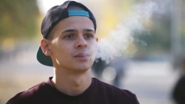 Mutlu esmer adam, güzel bir parkta, sonbaharda, güneşli bir yaz gününde güneşli bir parkta ayakta durup elektronik sigara yakan genç bir esmer adama ilham veriyor..