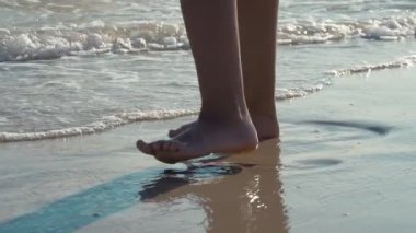 Güneşli bir yaz gününde, ıslak kumlu bir sahil sahilinde, güneşli bir yaz gününde, genç kadınların ayaklarının ıslak ve kumlu bir sahilde, yavaş çekimde ayakta ve yürüyor olması heyecan verici. İlham verici ve güzel görünüyor..