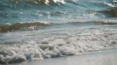 Işıl ışıl deniz dalgaları, güneşli bir günde yavaş çekimde köpüklü su sıçratarak güneşli bir yazın güneşli bir gününde kumlu sahile vuran köpüklü ve parlak deniz dalgalarının güzel manzarasını oluşturur. İlham verici, neşeli ve iyimser görünüyor..