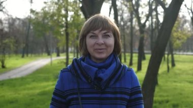 Romantik sarışın kadın, güneşli bir parkta ayakta ve gülümsüyor. Yavaş çekimde güneşli bir yaz gününde, parlak bir parkta durup gülümseyen, kısa saçlı, neşeli, sarışın bir kadının portresiyle.