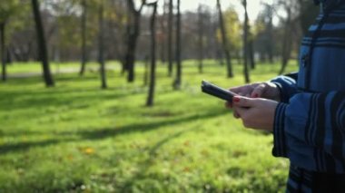 Bir kadının elleri akıllı telefonu tutuyor ve parkta ağır çekimde sörf yapıyor stil sahibi kadın ellerinin yakın plan çekimleri modern bir akıllı telefonu elinde tutuyor, internette geziniyor ve sonbaharda güzel bir parkta yavaş çekimde bazı bilgileri çeviriyor..