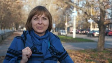 Güzel sarışın bir kadın, havadar bir parkta duruyor ve sonbaharda, mavi atkısı ve süslü ceketi olan, gülümseyen şık sarışın bir kadının ilham verici portresine bakıyor.