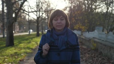 Sonbaharda ağaçlarla dolu bir park çitinde mavi atkısı ve ceketi olan ve yazın ağaçlarla birlikte beyaz bir park çitinde gezinen gülümseyen, şık, sarışın bir kadının iyimser görüntüsüyle yürüyen zarif sarışın kadın..