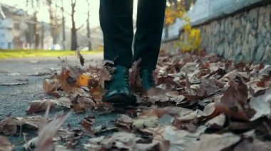 Zarif yüksek çizmeli kadın ayakları, paslı yaprakların üzerinde yürüyor. Yavaş çekim parkında. Yüksek topuklu, sarı çizmeli, zarif kadın ayaklarının iyimser yakın çekimi..