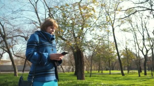Donna Bionda Intelligente Che Cammina Naviga Rete Telefono Nel Parco — Video Stock