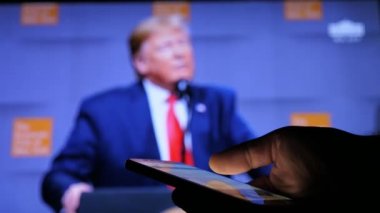 Kiev, Ukrayna - 8 Kasım 2019: Amerikan Başkanı Trump 'ın TV ekranında görülen muhteşem konsept görüntüsü. Dünya seyircilerine sesleniyor. Bir adamın eli bir akıllı telefonu profilde tutar ve kaydırır.   