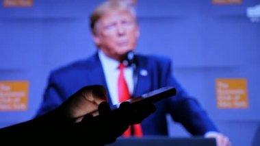 Kiev, Ukrayna - 8 Kasım 2019: Amerikan Başkanı Trump 'ın TV ekranında harika bir konsept görüntüsü. O, dünya seyircisiyle sohbet ediyor. Bir adamın el ele tutuşması ve profil içinde akıllı telefonu kaydırması.   