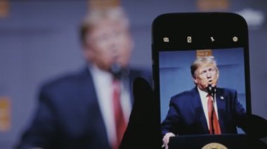 Kiev, Ukrayna - 8 Kasım 2019: Amerika Başkanı Trump 'ın muhteşem konsept görüşü bir televizyon ekranına yansıdı. Dünyayı ikna etmeye çalışıyor. Bir erkek eli de kendi görüntüsüyle akıllı telefon bulundurur..