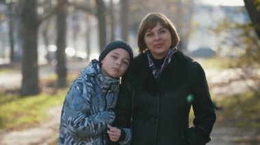 Kendine güvenen sarışın anne ve zeki oğlu güz mevsiminde güneşli bir sokakta mutlu bir aile manzarası izliyorlar. Zarif ceketli neşeli sarışın anne yürekten gülümsüyor. 11 yaşındaki oğlu sonbaharda açık havada omzuna yaslanıyor.