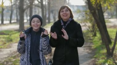 Mutlu sarışın anne ve 11 yaşındaki oğlu sonbaharda bir sokakta dans ediyor şık bir ceketle gülümseyen sarışın bir anne ve 11 yaşındaki oğlunun sonbaharda uzun ve düz bir sokakta mutlu bir şekilde dans edişlerinin neşeli görüntüsü..