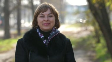 Sonbaharda zarif bir ceketle dışarıda dikilen ve gülümseyen hoş sarışın kadın. Şık bir palto giymiş, renkli bir atkısı olan ve sonbaharda dışarıda kendini iyi hisseden başarılı, sarışın bir kadının neşeli portresi..