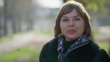 Sonbaharda şık bir paltoyla dışarıda dikilen ve gülümseyen zeki sarışın kadın, sonbaharda açık havada duran ve hayatın tadını çıkaran renkli eşarplı, kısa saçlı, kendine güvenen sarışın bir kadının portresi..