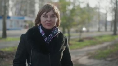 Başarılı sarışın kadın, güz mevsiminde şık bir paltoyla sokakta dikiliyor ve gülümsüyor. Şen şakrak, kısa saçlı, renkli atkısı olan ve sonbaharda caddeden uzağa bakan neşeli, sarışın bir kadının portresini çiziyor..