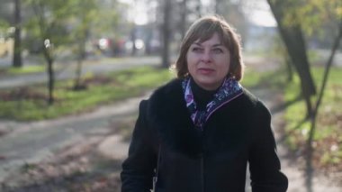 Sonbaharda bir sokakta şık bir paltoyla dikilen ve gülümseyen güzel sarışın kadın. Şık bir palto giymiş, renkli bir atkısı olan mutlu, sarışın bir kadının bokeh portresi. Sonbaharda uzak bir caddede dikiliyor..