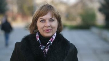 Neşeli sarışın kadın, sonbaharda parkta bir parkın içinde durmuş ve gülümsüyor. Kendine güvenen, kısa saçlı, renkli atkısı olan sarışın bir kadının portresi. Sonbaharda bir parkta dikiliyor ve öne doğru dönüyor..