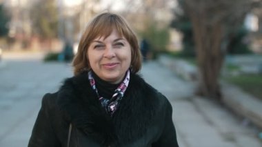 Sonbaharda bir parkta şık bir ceketle dikilen ve gülümseyen mutlu sarışın kadın. Şık bir palto giymiş, zarif bir saç kesimi olan, güzel bir parkta duran ve mutlu bir şekilde gülümseyen, kendine güvenen sarışın bir kadın..