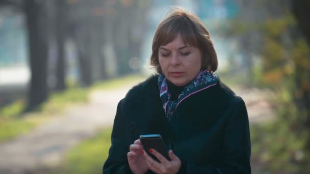 Zarif Ceketli Sarışın Kadın Sonbaharda Bir Caddede Akıllı Telefondan Arıyor — Stok video