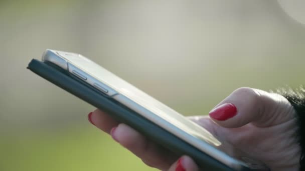 Main de femme avec un maquillage rouge touchant l'écran du smartphone dans une rue en automne Magnifique vue bokeh de la main d'une femme avec un maquillage rouge mauve textant sur un smartphone dans une rue en automne. Il semble joyeux, original et technologique 