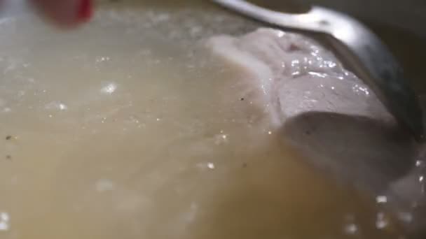 金属勺子把一大块白肉放在一个大砂锅里煮沸 在一个大的金属砂锅上用开水煮熟的大块白肉的令人印象深刻的特写中移动 一只金属勺子在左右搅拌 — 图库视频影像