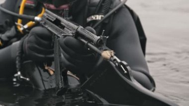 Odessa, Ukrayna - 11 Ekim 2019: Siyah dalış kıyafeti, dalış maskesi ve yüzgeçli bir yüzücüyü sersemleten, otomatik tüfeği ve paletleri elinde tutan ve yazın nehirde duran