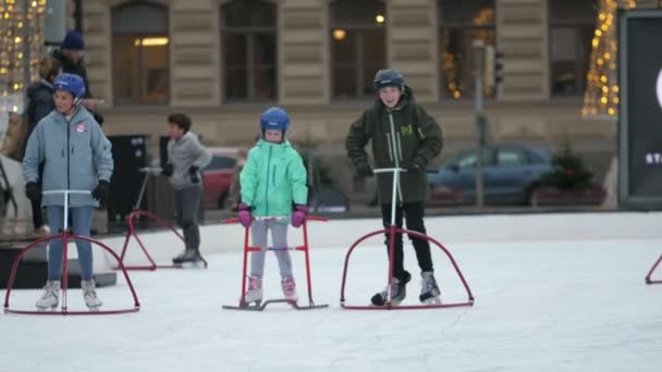フィンランド ヘルシンキ 2019年12月12日 冬の昼間にヘルシンキの伝統的な高層ビルに設置された大きなオープンアイスリンクで チューブスタンドスケートをしているいくつかの子供たちの陽気な景色 — ストック動画