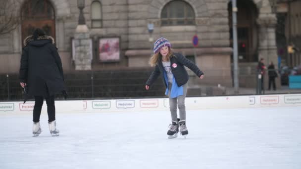 フィンランドのヘルシンキ 12月12 2019 遅い動きで冬にヘルシンキのリンク上のオープンアイスリンクで他の子供たちと気まずいスケートをしようとしている小さなブロンドの女の子の陽気な景色 — ストック動画