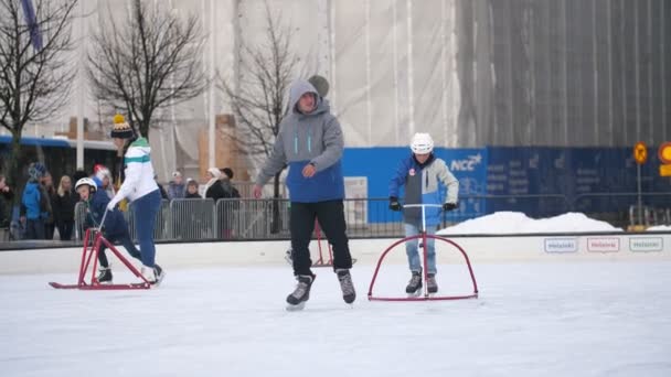 フィンランドのヘルシンキ 2019年12月12日 冬のフィンランドのオープンアイスリンクでゆっくりとした動きでチューブスタンドアイススケートをサポートするスポーツ大人とその子供たちの印象的な景色 — ストック動画
