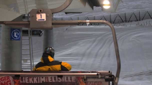 レヴィ フィンランド 2019年12月10日 ヘルメットで陽気なスキーヤーと雪の冬にフィンランドのレヴィスキーリゾートのスキーリフトのベンチに座っている大きなガラスの元のバックビュー — ストック動画