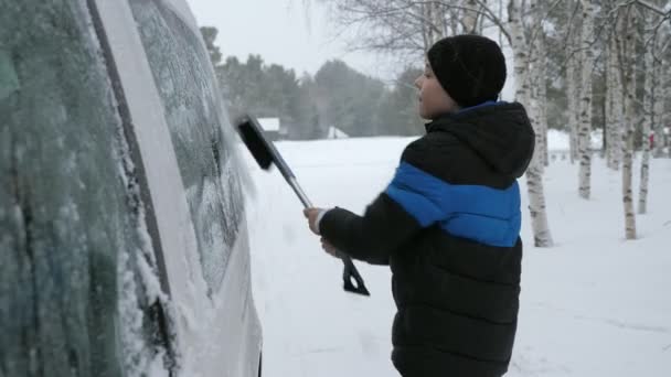 中国日报 的报道 芬兰一名积极的男孩在雪地的森林里把雪从汽车的侧窗上移开 看到一个快乐的11岁男孩在冬天把一辆被厚厚的雪覆盖在松木上的汽车的侧窗移走和擦干净 — 图库视频影像