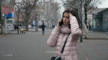 Sonbaharda bir caddede telefonla konuşan romantik esmer bir kız. Yavaş çekimde, güzel esmer bir kız. Uzun, gevşek saçlı, ayakta duran, akıllı bir kız.