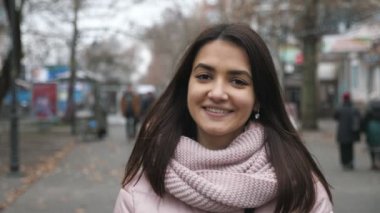 Neşeli esmer kız güz mevsiminde insanlarla dolu bir sokakta duruyor ve gülümsüyor. Parlak ve romantik gözlü güzel esmer bir kız portresi içinde. Uzun, gevşek saçlar ayakta ve güler yüzlü.