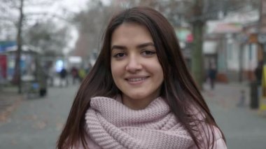 Çekici esmer kız, güz mevsiminde ağaçlarla dolu bir sokakta ayakta duruyor ve gülümsüyor. Güzel, stil sahibi, mutlu gözlü, uzun, bol saçlı, ayakta duran, gülümseyen ve gülen bir kızın portresi. Sonbaharda ağaçlarla dolu bir sokakta..