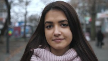Ağaçlarla dolu bir sokakta ayakta duran ve gülümseyen güzel esmer kız. Ağaçlarla dolu bir sonbaharda ağaçlarla dolu bir sokakta ayakta duran ve gülümseyen beyaz saçlı çekici bir kızın harika portresi. Biraz yorgun görünüyor..