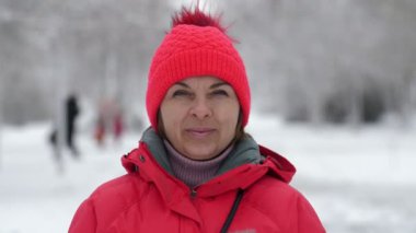 Kış mevsiminde Ukrayna 'da parlak bir parkta gülümseyen ve ayakta duran canlı sarışın kadın pembe şapkalı ve ceketli neşeli sarışın bir kadının kışın karlı bir çam parkında ağır çekim ağaçlarıyla gülümsemesi ve kendini harika hissetmesi.